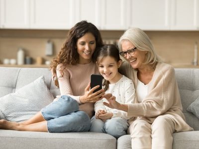 Cheerful mother, grandma and kid using digital gadget, Internet service, online application on smartphone together, enjoying modern technology, communication, leisure at home