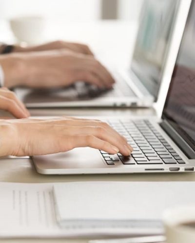 Close up image of female and male employers hands typing together on laptop keyboards at desk. Financial experts monitoring economical indicator online. E-commerce business team daily computer routine